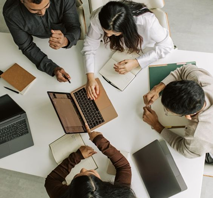 Люди работают за столом с ноутбуками и документами на совещании